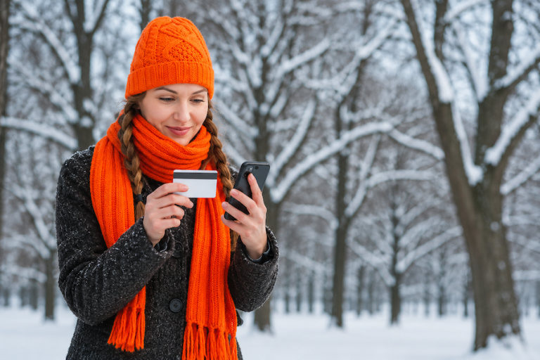 Woman outside in winter paying online credit card bill. Wearing hunting orange hat and scarf.